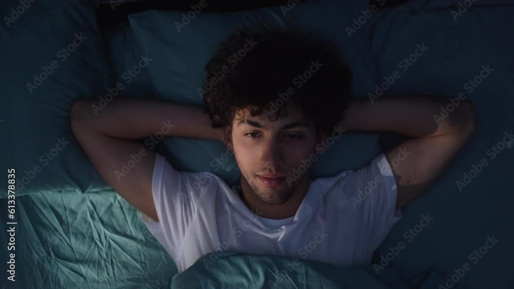 Stressed young man trying to sleep in his bed at night, suffering insomnia Stressed young man trying to sleep in his bed at night, suffering insomnia