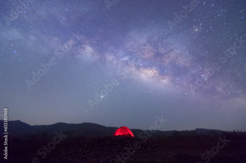 Red tent in reservoir under Milky way galaxy with stars and space dust in the universe, long speed exposure with noise. Baan Sop pat, Mae Moh Lampang Thailand.