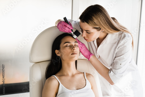 Dermatoscopy of skin lesions and moles with dermatoscope for preventing skin cancer and melanoma. Dermatologist examines moles and birthmarks of girl patient using dermatoscope.