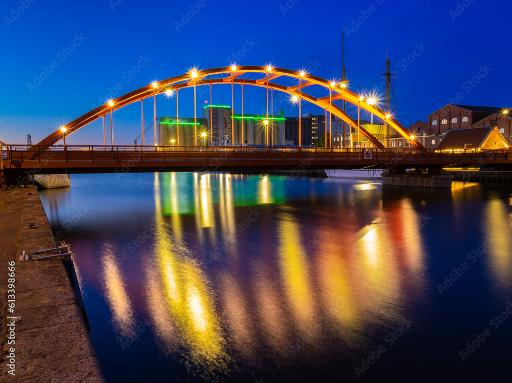 Fototapeta premium The red semi-circular railway bridge over the canal in Lidkoping in the glowing blue hour lighting and colorful reflections