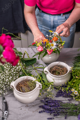 Florist bei der Arbeit, Frau steckt ein Blumengesteck aus frischen bunten Blumen in Gefäße aus Keramik