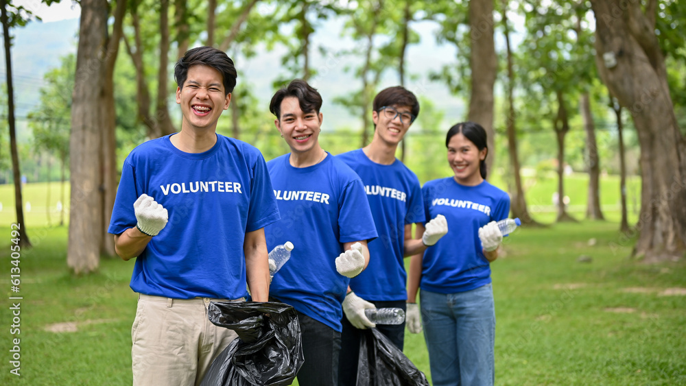 A group of Asian volunteers with garbage bags are standing in the park and showing their fists. A group of Asian volunteers with garbage bags are standing in the park and showing their fists.