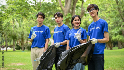 A group of happy Asian volunteers in uniform stand in a public park with plastic garbage bags