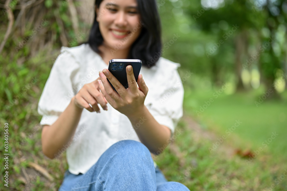 A beautiful young Asian woman using her smartphone while relaxing in a park. A beautiful young Asian woman using her smartphone while relaxing in a park.