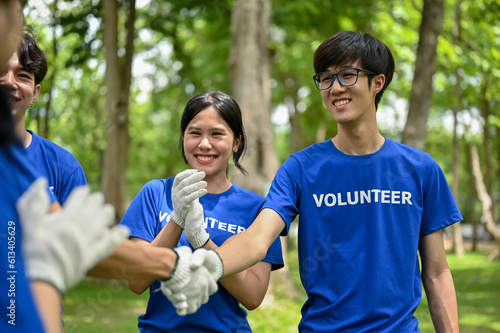 A happy Asian male volunteer shakes hands with his team after finishing volunteer work in the park.