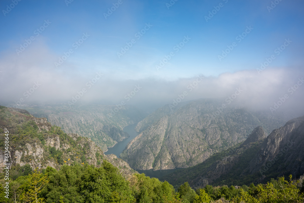 panoramic aerial view with a drone from the top of the Sil Canyon, in the Ribeira Sacra, Galicia, with the mountains on the sides of the river and thick fog over them.
