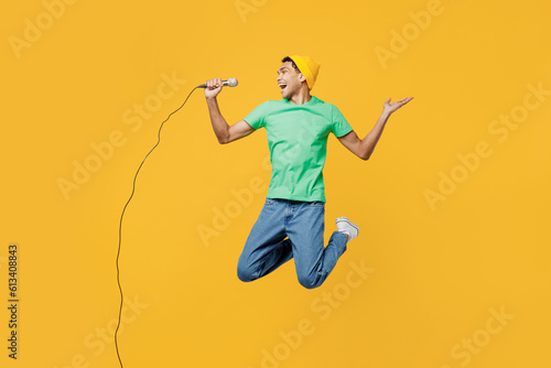 Full body young man of African American ethnicity he wearing casual clothes green t-shirt hat jump high sing song in microphone isolated on plain yellow background studio portrait. Lifestyle concept. photo
