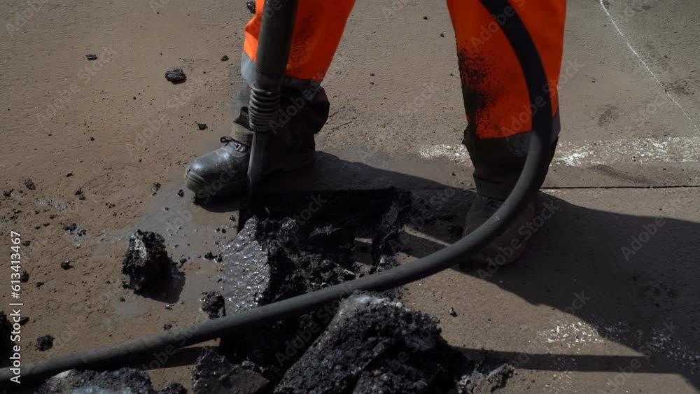 A worker removes old asphalt with a jackhammer A worker removes old asphalt with a jackhammer