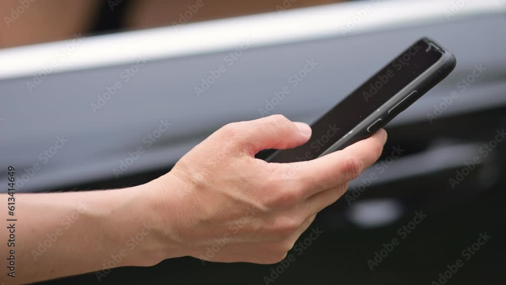 Lady car owner scrolls social media and news update on black smartphone. Businesswoman uses phone in modern black car standing at traffic jam Lady car owner scrolls social media and news update on black smartphone. Businesswoman uses phone in modern black car standing at traffic jam
