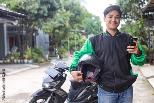 Portrait of Asian online taxi driver wearing green jacket holding helmet and smartphone © Gatot