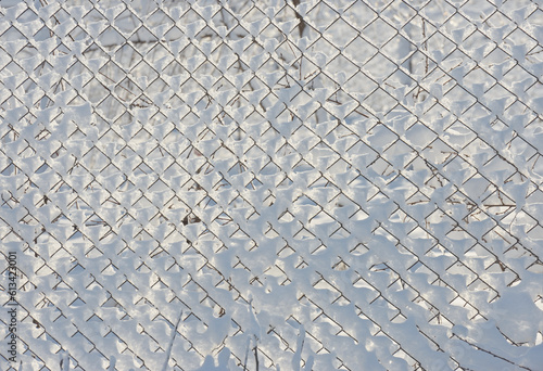 Many cells of chain-link fence are covered with fresh snow.