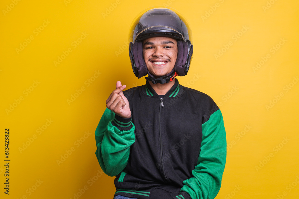Asian online taxi driver wearing green jacket and helmet showing heart sign over yellow background Asian online taxi driver wearing green jacket and helmet showing heart sign over yellow background