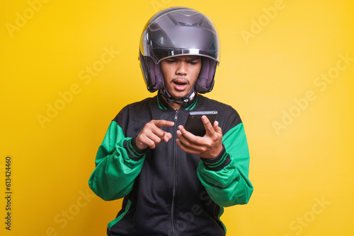 Shocking Asian online taxi driver wearing green jacket and helmet pointing finger to his smartphone 