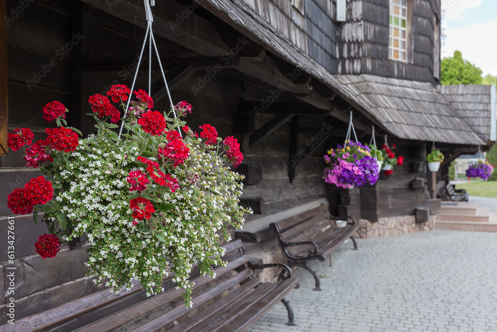 Flowerpots with different flowers suspended under roof of wooden church