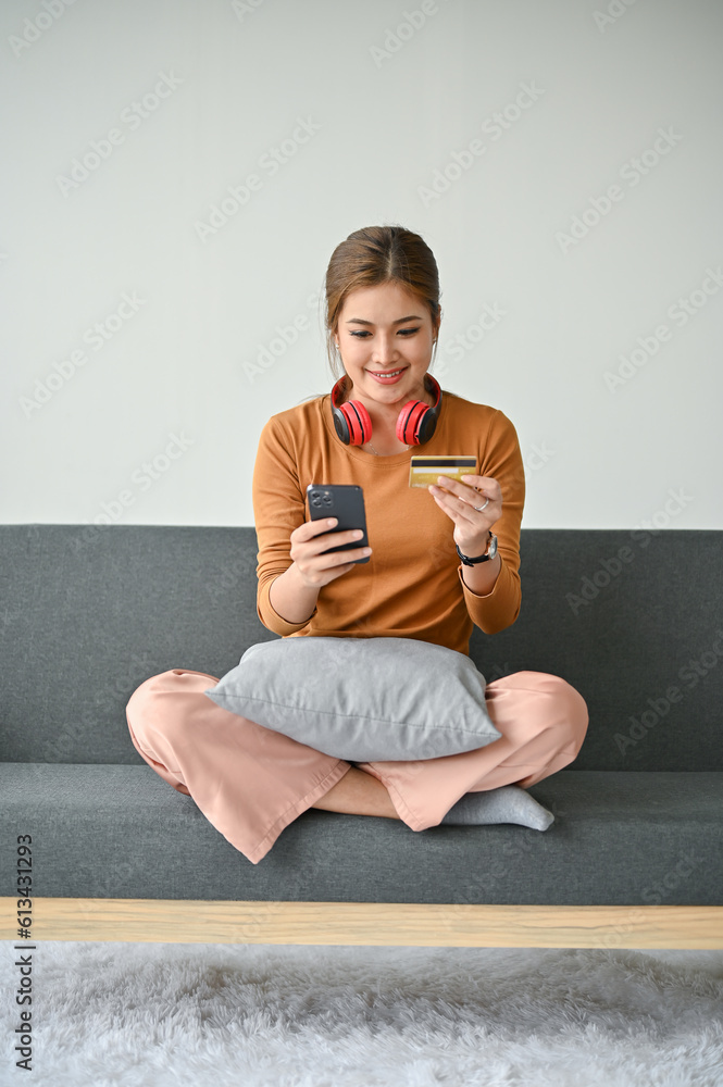A woman enjoys shopping online at home, paying her online bills through her smartphone. A woman enjoys shopping online at home, paying her online bills through her smartphone.