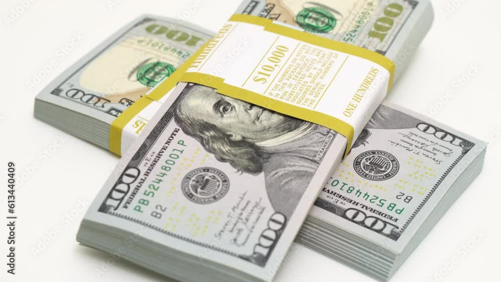stack of bank bundles with US dollars on a white background. Close-up shot of new, freshly printed hundred-dollar bills rotating on a table. cash flow, business investment, or big money concepts. stack of bank bundles with US dollars on a white background. Close-up shot of new, freshly printed hundred-dollar bills rotating on a table. cash flow, business investment, or big money concepts.