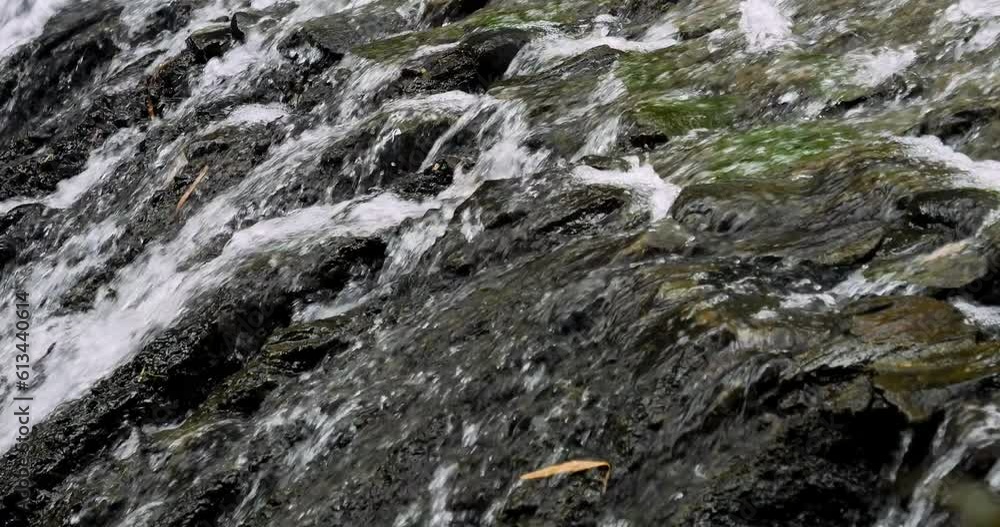 Close up slow motion shot of a flowing waterfall with view of the stones in bali indonesia Close up slow motion shot of a flowing waterfall with view of the stones in bali indonesia