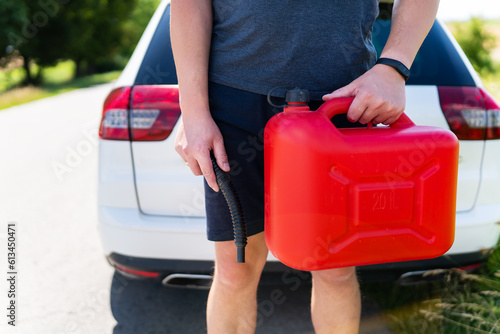 A man holds a red canister near a white car  close-up. Stop to refuel  no refueling  fuel problems.