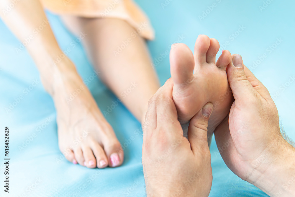 Fototapeta premium Male masseur massaging feet to young relaxing woman lying on blue massage table, close-up. Concept of massage spa treatments. Professional physiotherapist with strong hands performing foot massage.