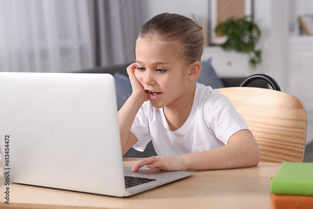 Little girl using laptop at table indoors. Internet addiction