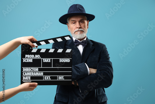 Senior actor performing role while second assistant camera holding clapperboard on light blue background. Film industry photo