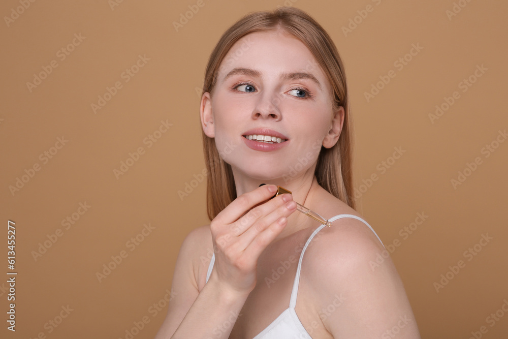 Beautiful young woman applying essential oil onto shoulder on brown background Beautiful young woman applying essential oil onto shoulder on brown background