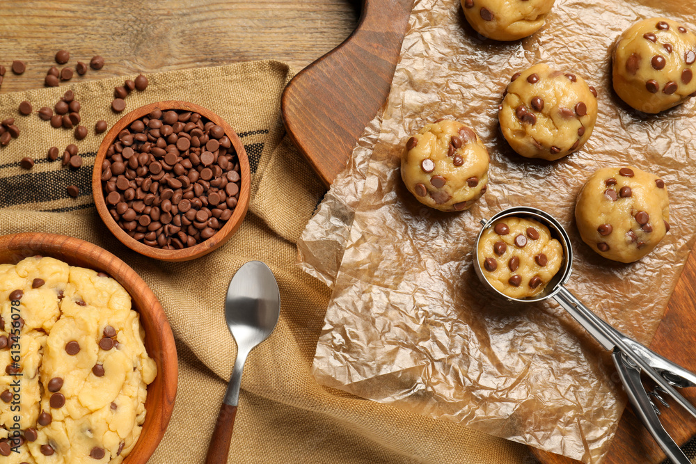 Fototapeta premium Bowl with dough and uncooked chocolate chip cookies on wooden table, flat lay