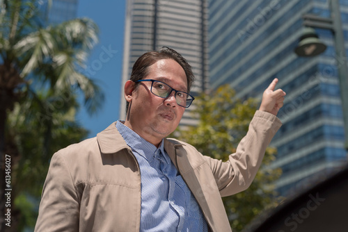 A middle aged asian office worker in his 40s nonchalantly pointing to his place of work. Urban city background.