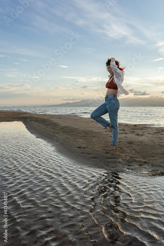 woman on the beach dancing at sunset in backlight with the sun behind in shadow, woman on vacation walking on the sand with golden water reflections from the sun at sunset