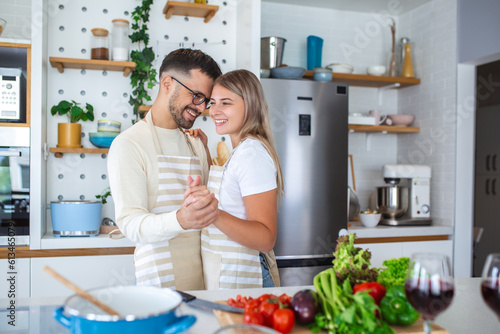 Overjoyed young family having fun in modern kitchen, dancing and laughing, happy young wife and husband moving to favorite music, enjoying leisure time, cooking dinner together, romantic date