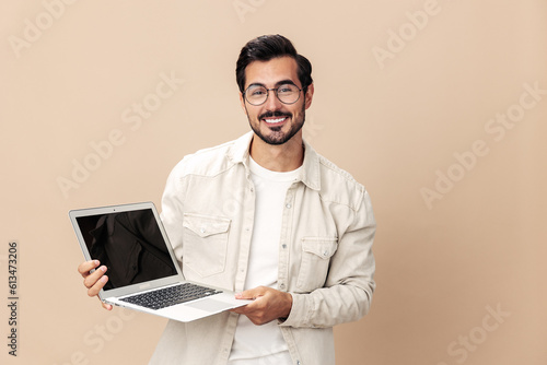 Portrait of a stylish with a laptop in his hands mockup, working freelancer smile with teeth open mouth, on a beige background in a white t-shirt, fashionable clothing style, space space