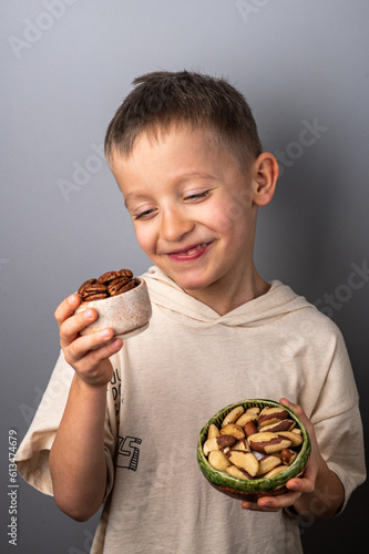 Cheerful little boy chooses between different nuts. Peeled pecan and Brazil nut. Healthy Eating.
