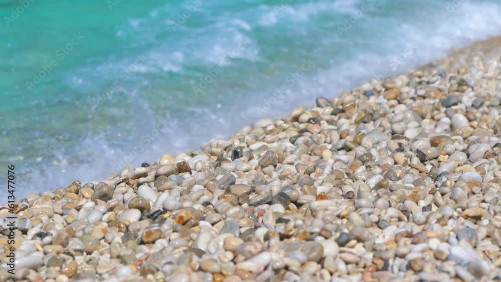 Closeup detail - small pebbles or rough sand on a beach, blurred afternoon sun lit calm sea in background, camera pan slowly Closeup detail - small pebbles or rough sand on a beach, blurred afternoon sun lit calm sea in background, camera pan slowly