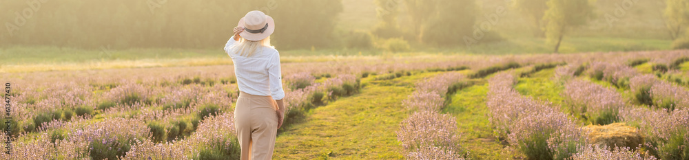 Beautiful young healthy woman with a white dress running joyfully through a lavender field holding a straw hat under the rays of the setting sun