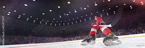 Dynamic image of young man, professional hockey player in uniform on 3D ice rink arena in motion with stick and puck. Blurred audience, fans. Sport, competition, match, game, action and motion concept