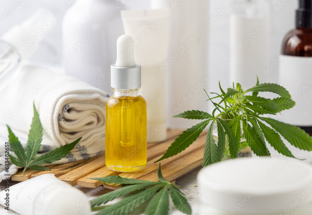 Dropper bottle with CBD oil near green cannabis leaves near bottles and towel close up