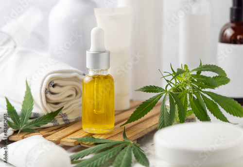 Dropper bottle with CBD oil near green cannabis leaves near bottles and towel close up