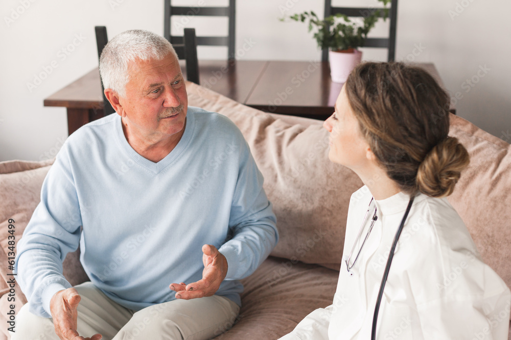 Female professional doctor showing medical test result explaining prescription using clipboard visiting senior elderly old man patient at home sitting on sofa