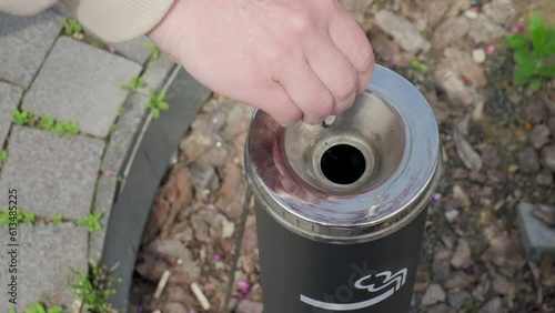 Smoker hand throws cigarette butt into street ashtray in designated outdoor smoking area.