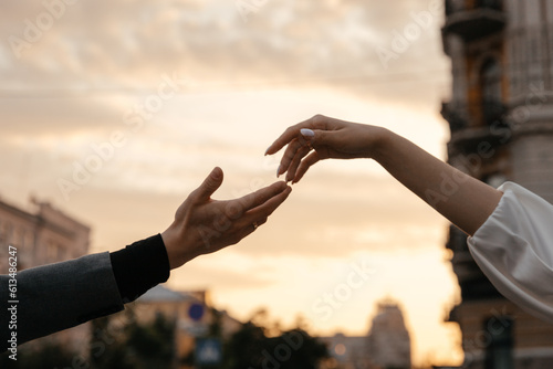 The hands of the bride and groom reach for each other against the background of the sunset