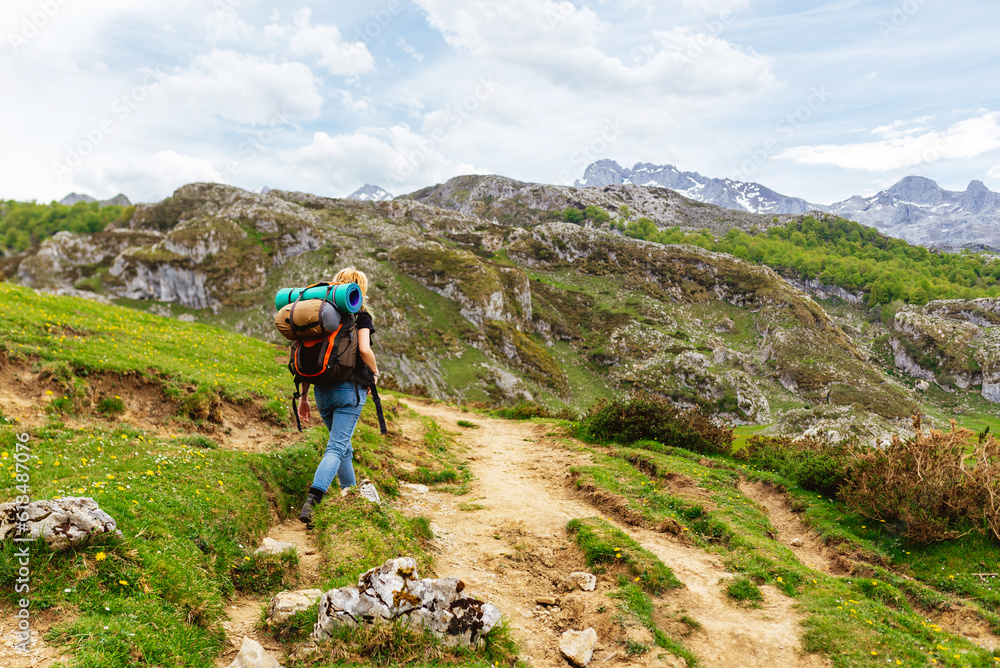 Hiker woman equipped with backpack, sleeping bags and bivouac mat, walking up the mountain in the Picos de Europa National Park, Asturias, Spain. Sport and outdoor adventure.