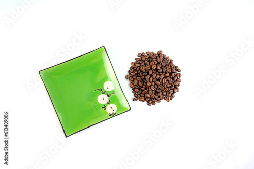 A pile of coffee beans next to a square green saucer, white background