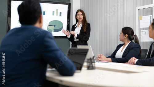 Businesswoman standing in conference room giving statistic presentation. Young Asian professional business woman talking, presenting strategy planning to executive working team in corporate meeting.