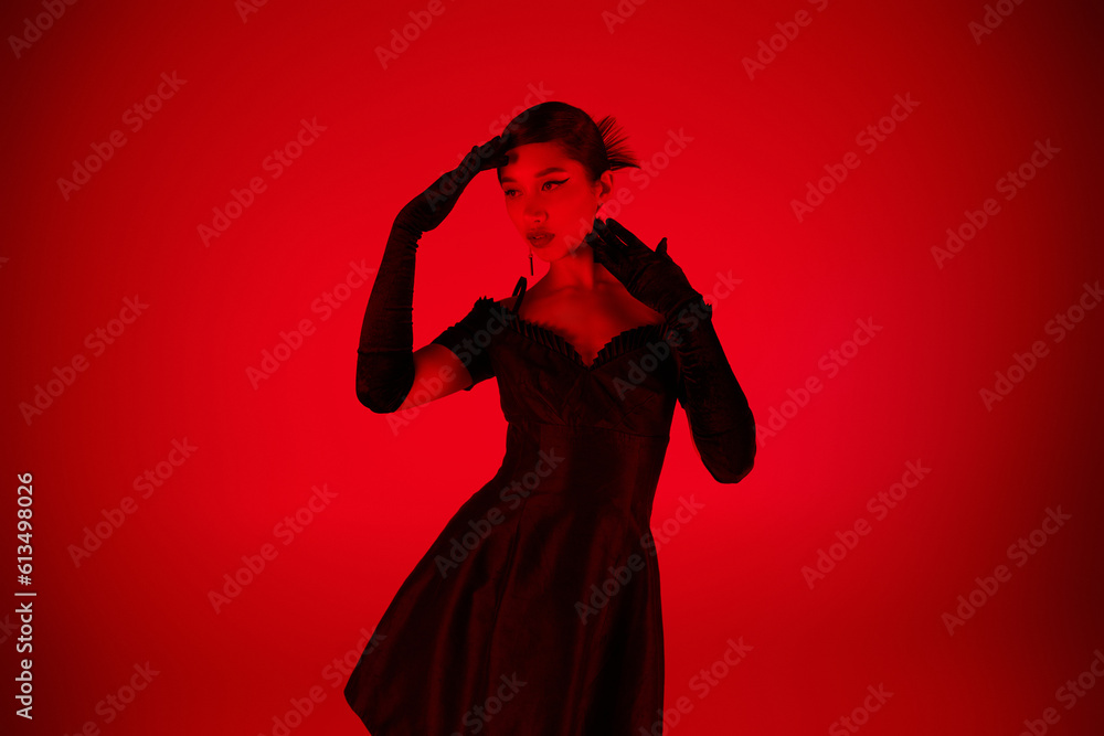 young asian woman in black long gloves and elegant cocktail dress standing in expressive pose and looking away on vibrant background with red lighting effect, youth culture, fashionable spring young asian woman in black long gloves and elegant cocktail dress standing in expressive pose and looking away on vibrant background with red lighting effect, youth culture, fashionable spring