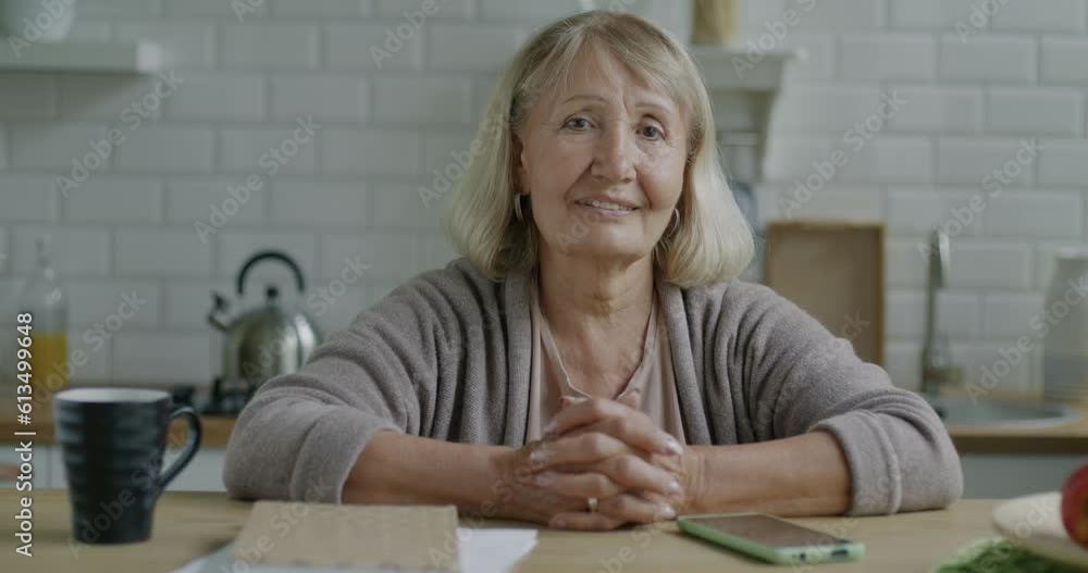 Slow motion portrait of senior woman smiling sitting at kitchen table at home. Retirement and positive emotion in apartment concept. Slow motion portrait of senior woman smiling sitting at kitchen table at home. Retirement and positive emotion in apartment concept.