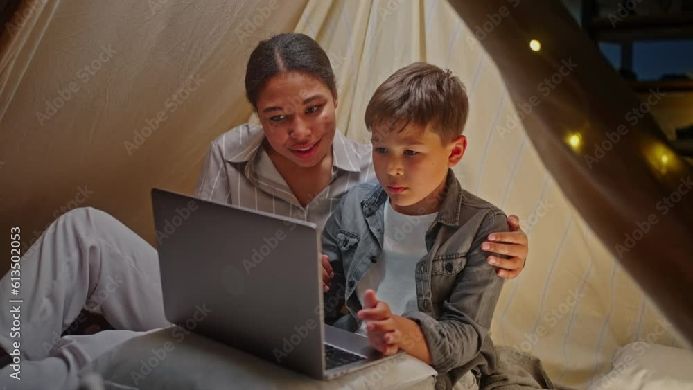 Loving mother and cute son have using laptop, browsing intenet sites, sitting inside a tent at home Loving mother and cute son have using laptop, browsing intenet sites, sitting inside a tent at home