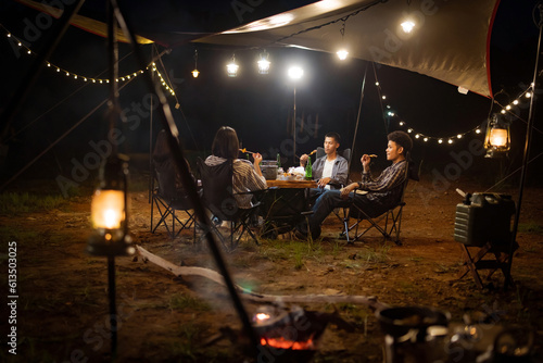 Young Asians eating barbecue under a canvas on a lake holiday evening having a tent under the lights.