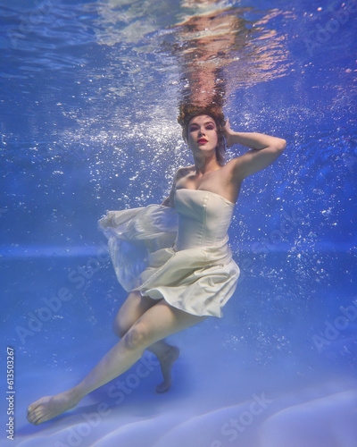 girl in a beautiful white dress underwater with flowers