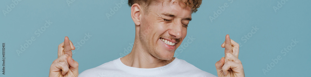 Obraz premium Young handsome hopeful man with closed eyes and crossed fingers