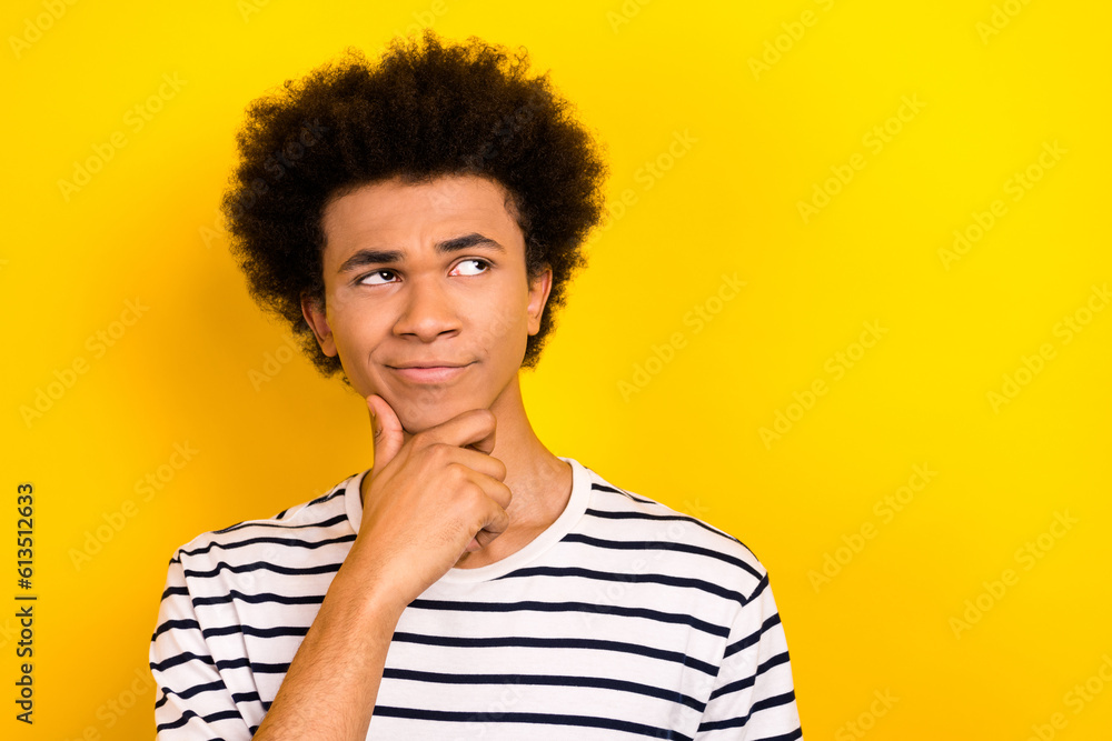 Portrait doubtful student guy look up hand on chin overthinking not sure wear striped t-shirt isolated yellow color background Portrait doubtful student guy look up hand on chin overthinking not sure wear striped t-shirt isolated yellow color background